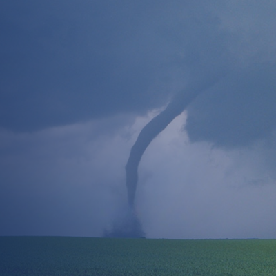 Tornado touching down over rural farmland beneath a dark stormy sky